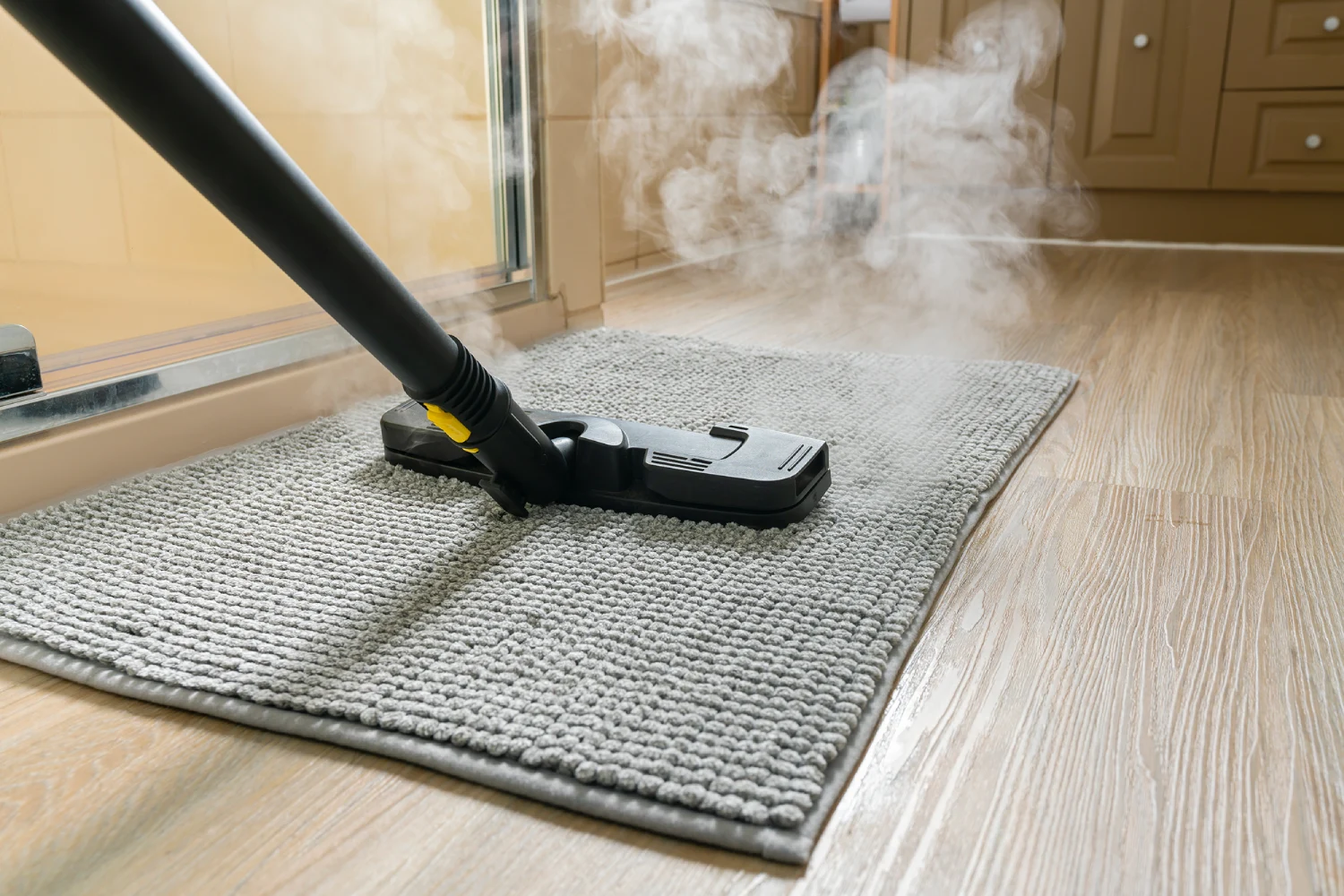 Steam cleaning a gray carpeted mat.