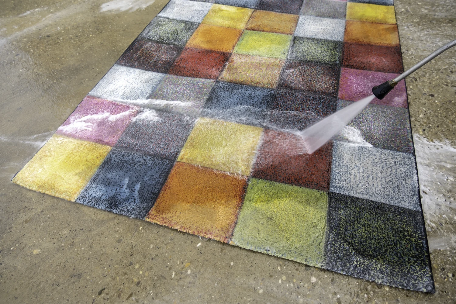 Washing colorful checkered carpet with pressure washer.